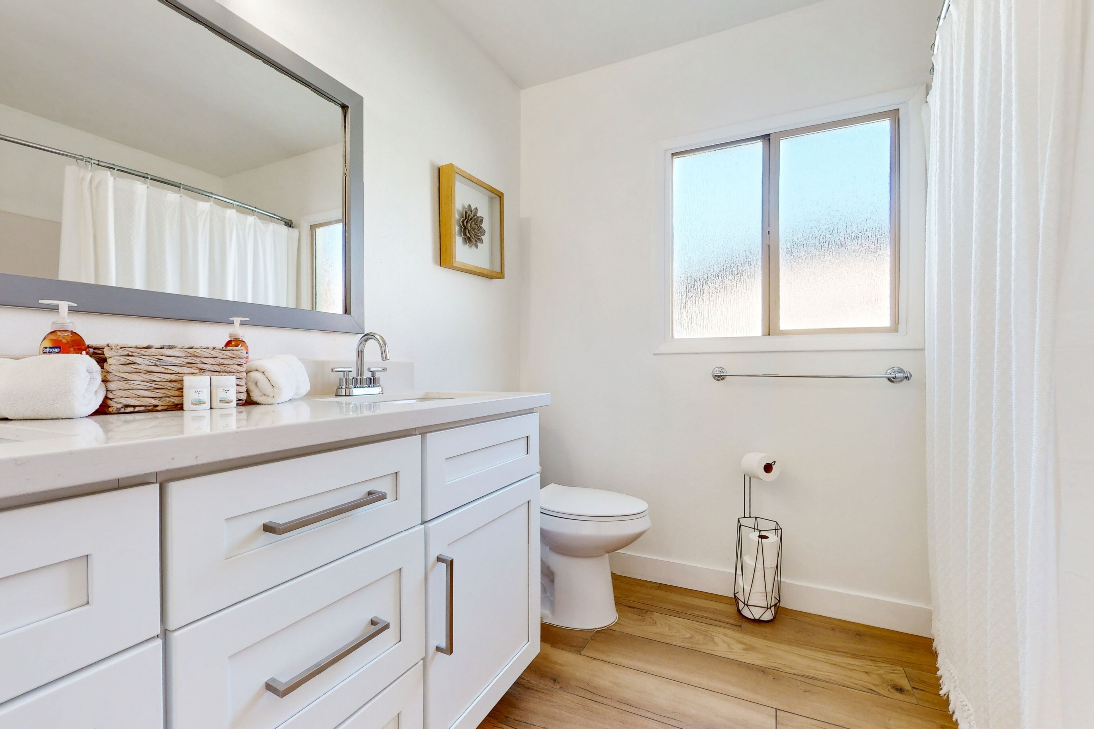 A bathroom with a white vanity, a toilet, a window, and a shower curtain.