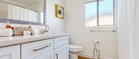 A bathroom with a white vanity, a toilet, a window, and a shower curtain.