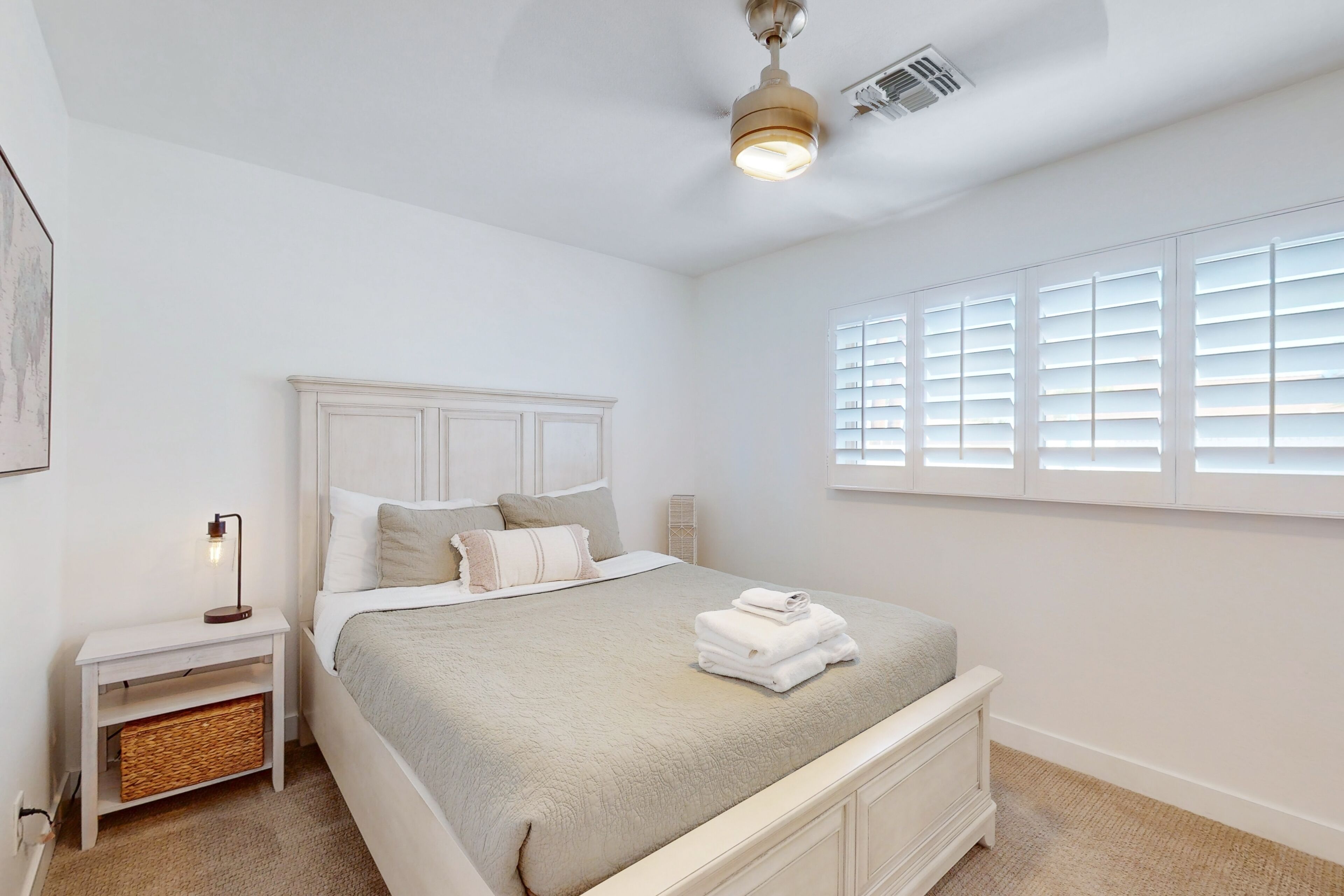 A bedroom with a bed, nightstand, bedside table, and a window with blinds.