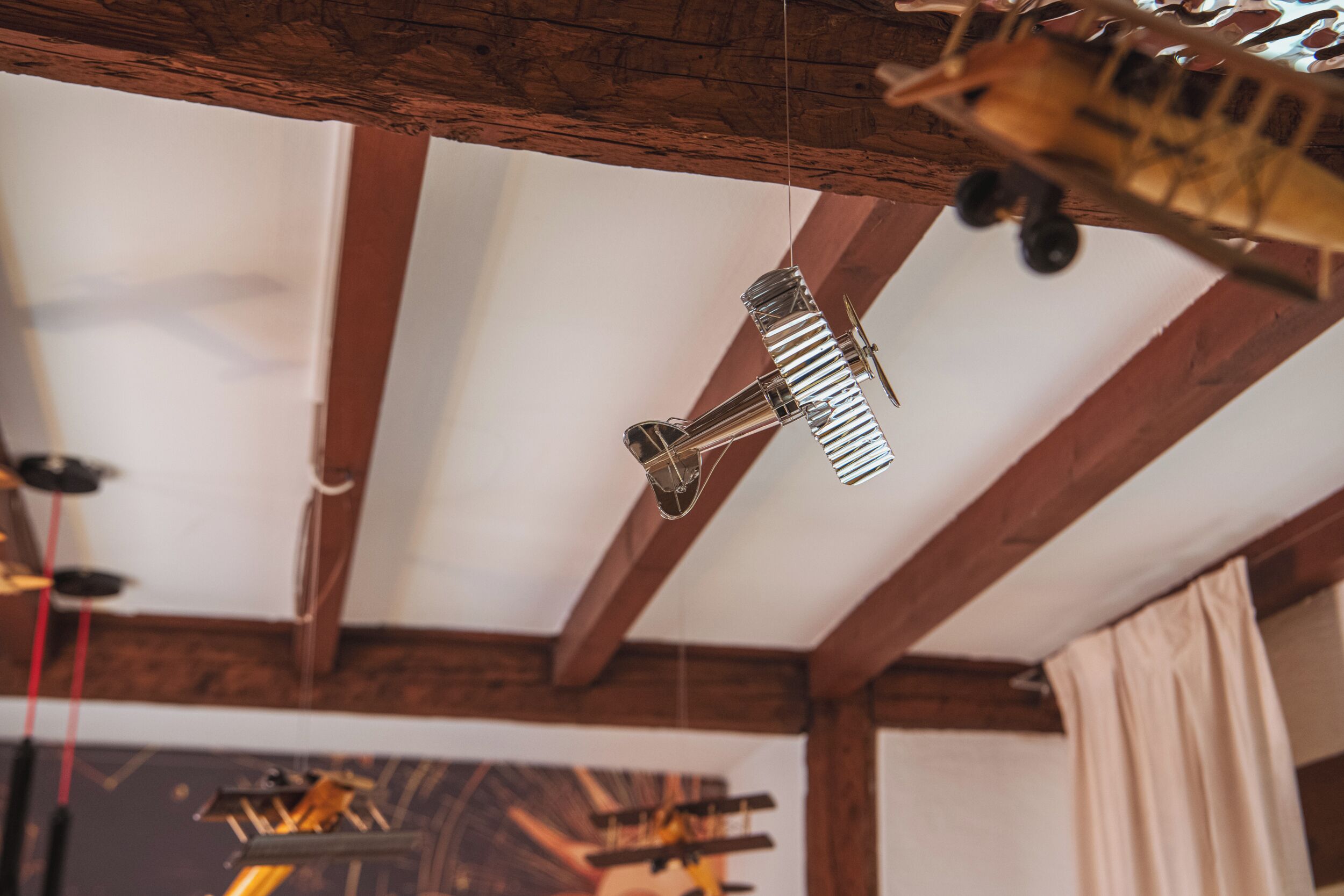 A room with exposed wooden beams, a hanging light fixture, and a painting on the wall.