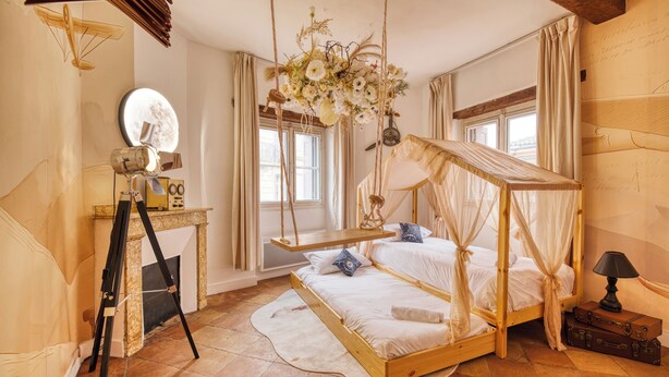 Una camera da letto con un letto a baldacchino in legno, una poltrona a dondolo sospesa, un treppiede e uno specchio.