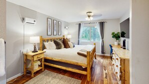 Une chambre à coucher avec un lit en bois, des tables de chevet, un bureau, une fenêtre avec des rideaux et un ventilateur de plafond.