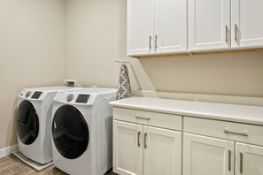 A laundry area with two front-loading washing machines, a countertop, and white cabinetry. - Modern townhome with private patio, grill, rooftop deck, on-site pool & gym (Scottsdale)