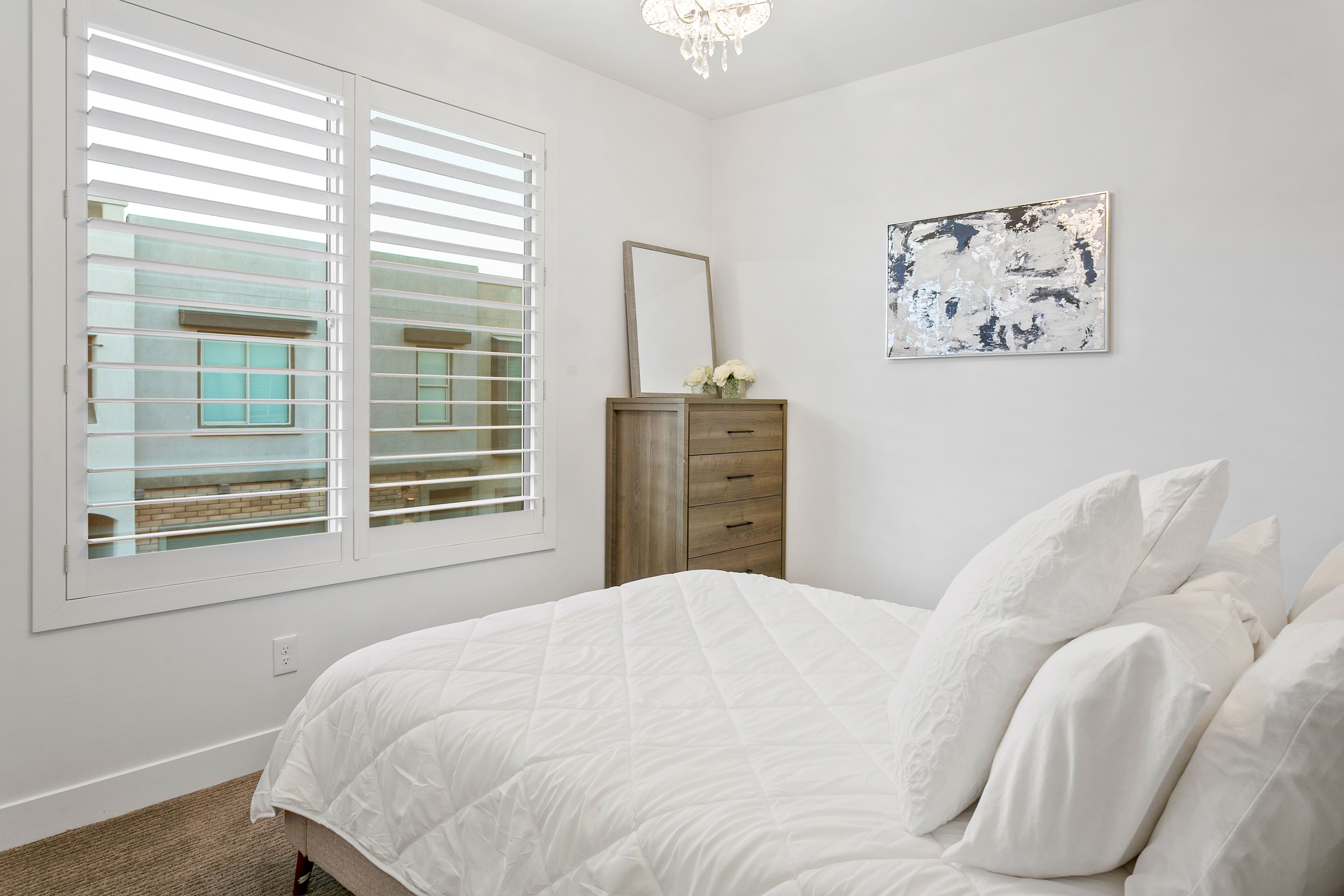 A bedroom with a bed, a dresser, a mirror, and a window with blinds.