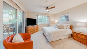 Une chambre à coucher comprenant un lit, un téléviseur, un ventilateur de plafond et une vue sur l’extérieur grâce à de grandes fenêtres.