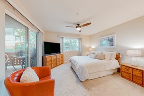 A bedroom with a bed, a TV, a ceiling fan, and a view of the outdoors through large windows. - Inviting mountain-view condo with balcony - hot tub, heated pool & golf on-site (Scottsdale)