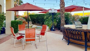 Une terrasse extérieure avec une table et des chaises, un barbecue et des parasols pour faire de l’ombre.