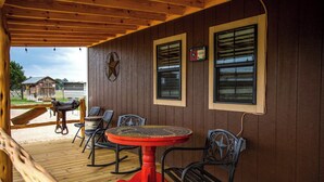 A covered outdoor seating area with a round table and four chairs, wooden deck flooring, and a wooden ceiling. - RRR Retreat | 2 Cabins | Medina Riverfront (Medina)
