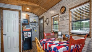 A room with a wooden ceiling, a white door, a refrigerator, a table with a red and white tablecloth, and a clock on the wall. - RRR Retreat | 2 Cabins | Medina Riverfront (Medina)