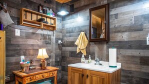 A wooden-paneled bathroom with a wooden vanity, a mirror, a towel hanging on the wall, and a sink with toiletries. - RRR Retreat | 2 Cabins | Medina Riverfront (Medina)