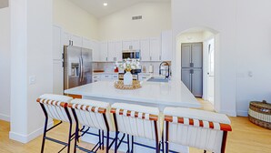 A modern kitchen with white cabinetry, a large island, and bar stools. - This charming, single-level home in Chandler is the ideal spot for families (Chandler)