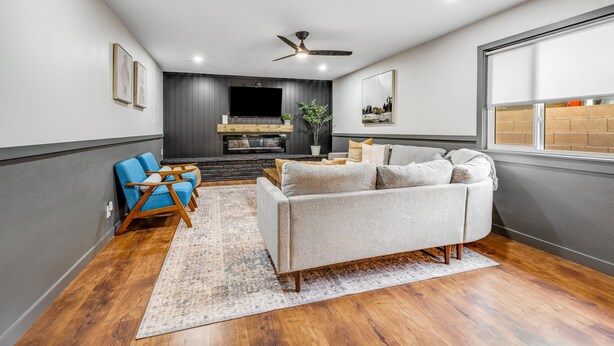 Ein Wohnzimmer mit grauem Sofa, blauen Sesseln, einem Holztisch und einem großen Teppich.