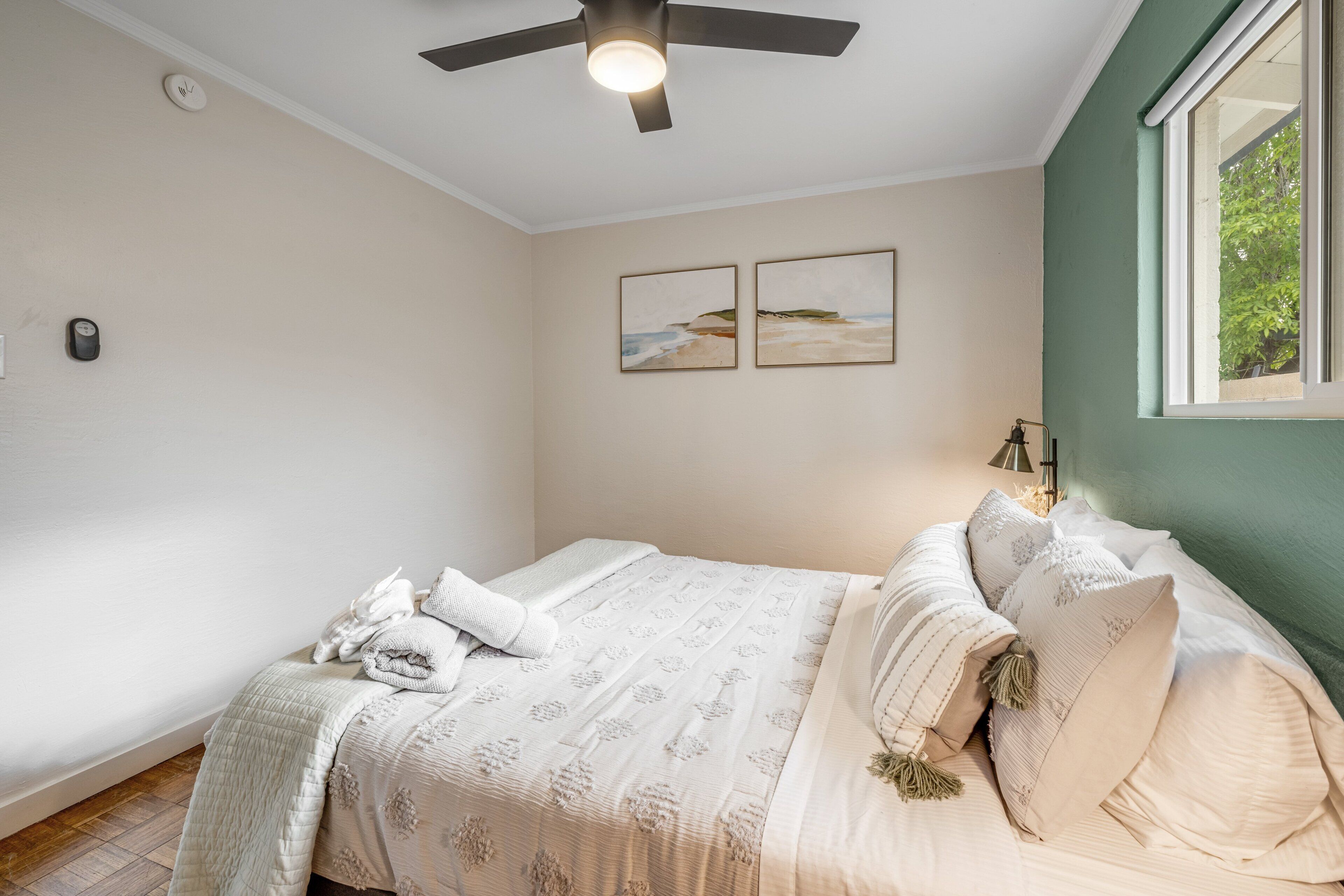 A bedroom with a bed, a ceiling fan, and two framed pictures on the wall.