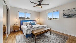 Ein Schlafzimmer mit Bett, Nachttischen, einer Bank, einem Deckenventilator und zwei Fenstern.