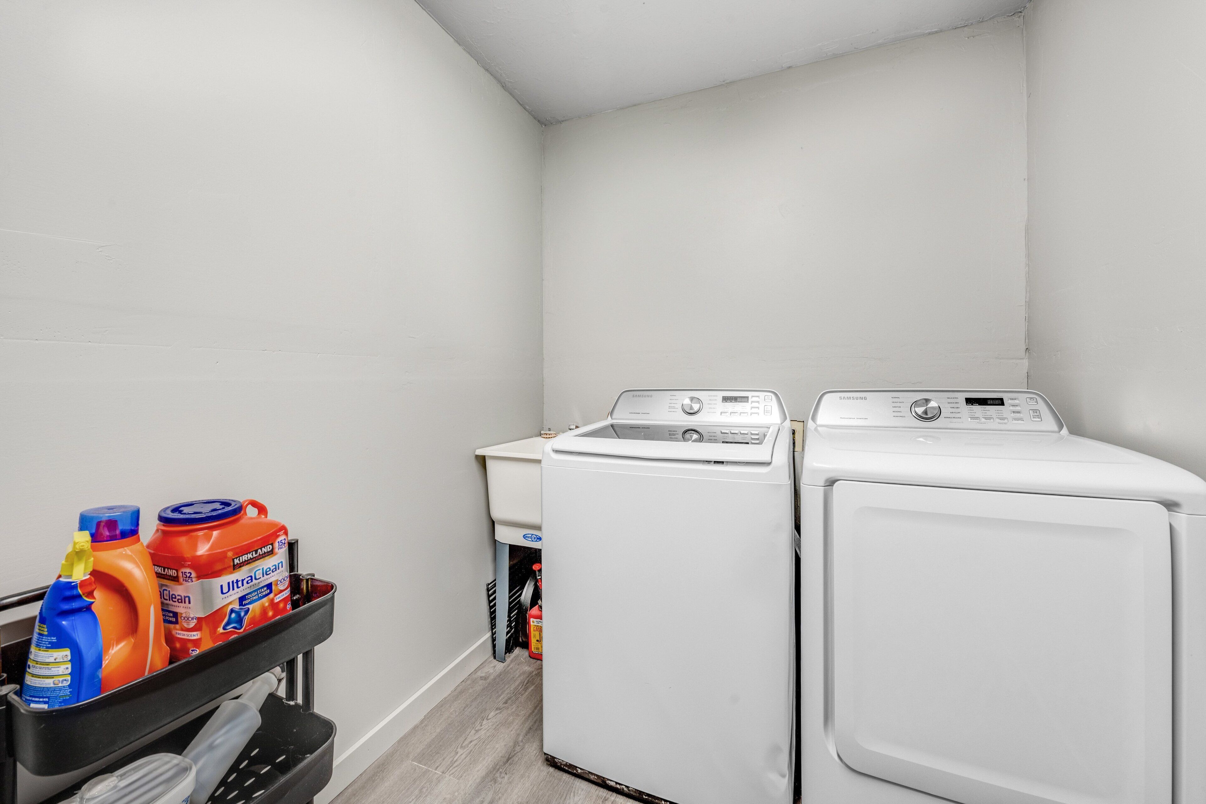 Un espace dédié à la buanderie, avec deux machines à laver blanches et un chariot contenant des produits de nettoyage.