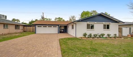 A single-story house with a garage, a paved driveway, and a small front yard with a lawn and a few shrubs.
