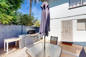 An outdoor patio with a grill, a table, chairs, and a covered umbrella.