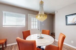 A dining area with a round table, four orange chairs, a chandelier, and a door with a window.