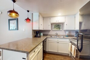 A modern kitchen with white cabinets, a stainless steel refrigerator, a coffee maker, and a sink. - Dog-friendly condo near attractions with fenced yard, central AC, and cute decor (Glendale)