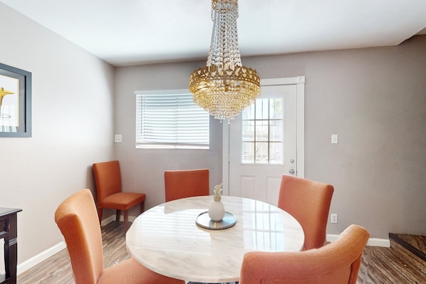A dining area with a round table, orange chairs, a chandelier, and a framed picture on the wall.