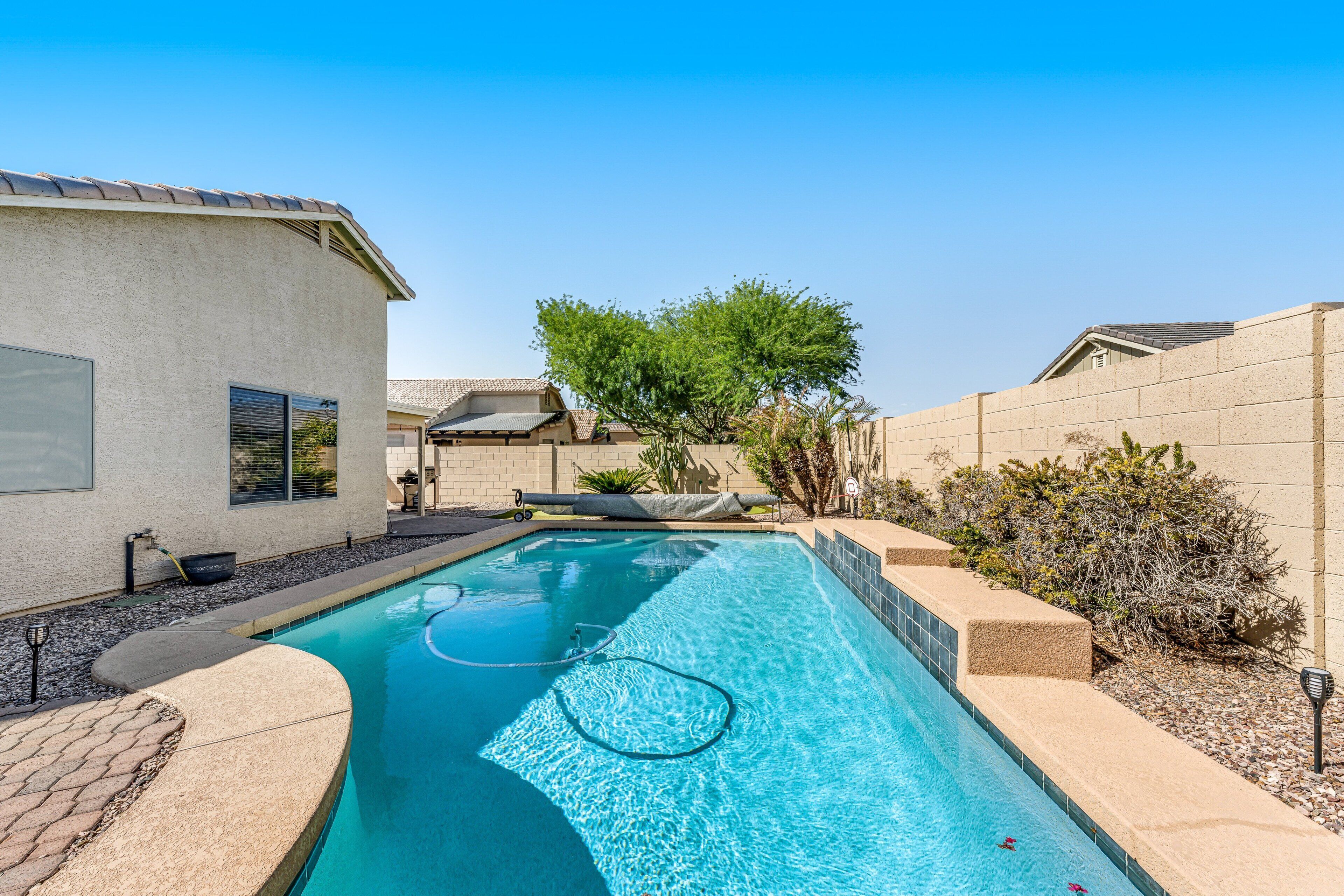 A swimming pool with a clear blue water surface, surrounded by a paved deck and a low stone wall.