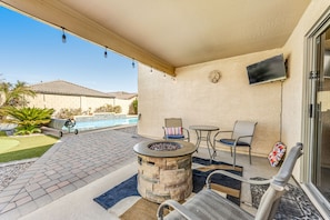 A covered patio with a stone fire pit, outdoor seating, a pool, and a TV mounted on the wall. - Spacious home with private heated pool with waterfall, putting green & firepit (Goodyear)