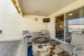 A patio area with a stone fire pit, outdoor seating, a television, and a view of a swimming pool.
