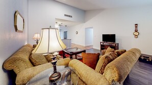 Ein Wohnzimmer mit einer Couch, einem Tisch mit Lampe, einem Fernseher und einer Wanduhr.