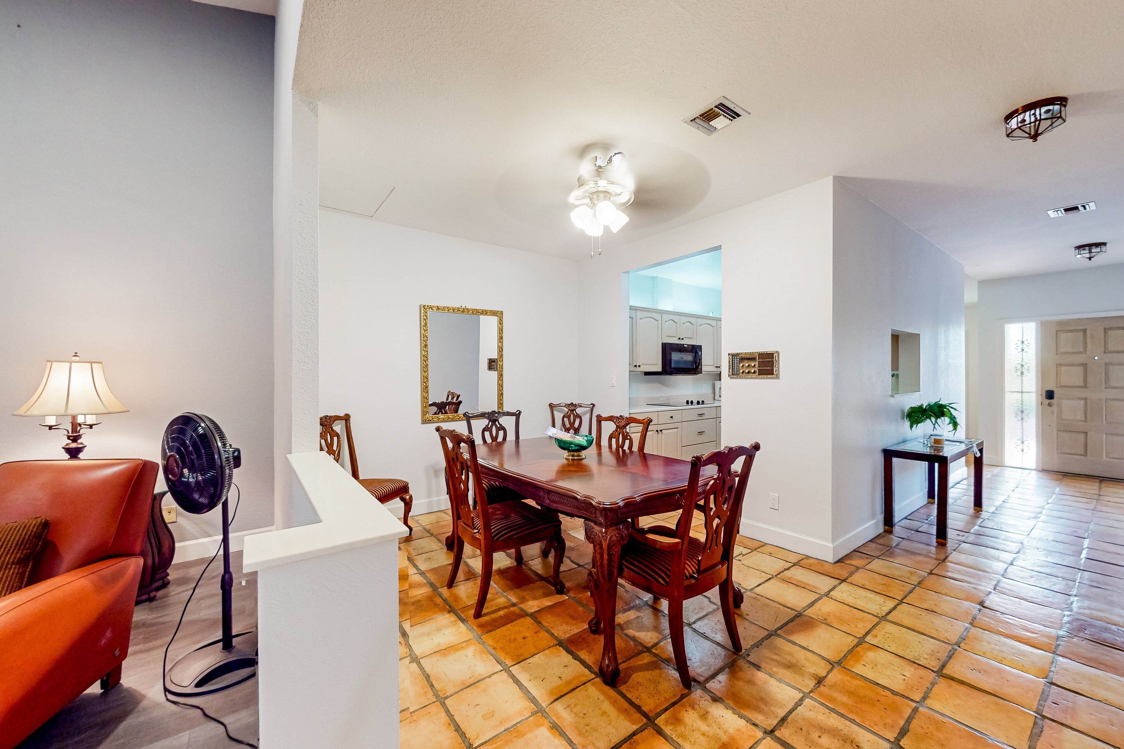 A dining area with a wooden table and chairs, a ceiling fan, and a kitchen in the background.