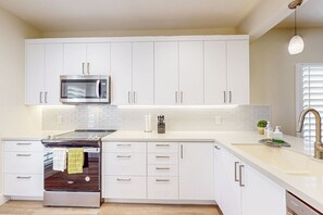 A modern kitchen with white cabinets, stainless steel appliances, and a white countertop.