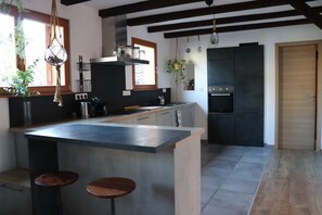 Uma cozinha moderna com uma ilha central, banquetas, uma geladeira preta e plantas penduradas.