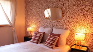 A neatly made bed with striped pillows, a bedside lamp, and a mirror on the wall.