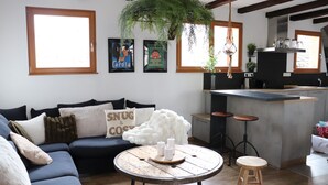 A modern living room with a dark blue sofa, a round wooden coffee table with candles, and a hanging plant.