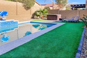 A swimming pool with artificial grass, a hot tub, and lounge chairs.