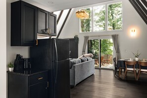 Una cocina moderna con un refrigerador negro, armarios de madera y una zona de comedor con una mesa para dos.