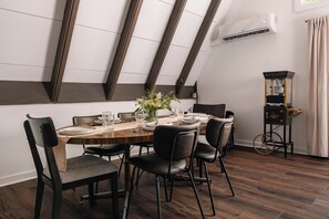A dining area with a wooden table set for six, surrounded by black chairs, in a room with sloped ceiling and exposed beams.