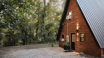 Een houten chalet met schuin dak, een grindpad en een omliggend bos.