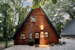 Una cabaña de madera con techo triangular, puerta principal y dos ventanas.