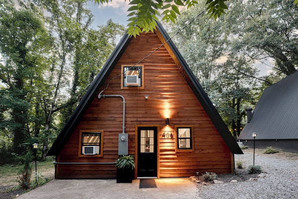 A wooden cabin with a triangular roof, a front door, and two windows.