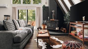 Een moderne woonkamer met een grijze bank, een houten salontafel, een zwarte open haard en een boekenkast.