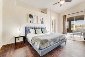 A bedroom with a large bed, a nightstand, a ceiling fan, and a view through a sliding glass door.