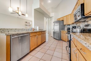A modern kitchen with granite countertops, stainless steel appliances, wooden cabinets, and a ceiling fan. - Modern Home w/ Private Pool, Central AC, WiFi, Private W/D, & Private Gas Grill (Goodyear)