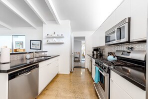Eine moderne Küche mit weißen Schränken, einer schwarzen Arbeitsplatte, Edelstahlgeräten und einer gefliesten Spritzschutzwand.