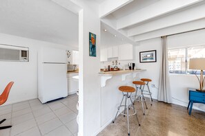 Eine moderne Küche mit weißen Schränken, einer zentralen Kochinsel mit Sitzgelegenheiten, einem Fenster mit Vorhängen und einem blauen Beistelltisch.