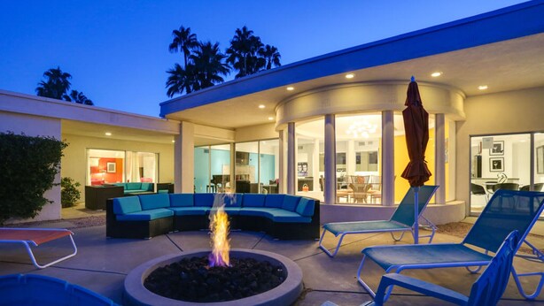 Eine Außenpatio mit Feuerstelle, blauen Lounge-Sesseln und einer gebogenen Sitzgruppe.