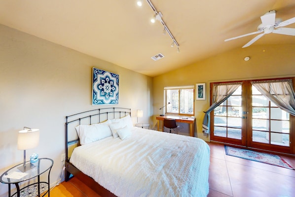 Une chambre à coucher comprenant un lit, un bureau, une chaise, un ventilateur de plafond et une fenêtre avec des rideaux.