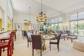 A spacious living room with a round glass coffee table, comfortable seating, and a large window offering a view of the outdoors. - Inviting PGA West Condo w/3 Golf Courses + Sparkling Pool & Hot Tub (La Quinta)