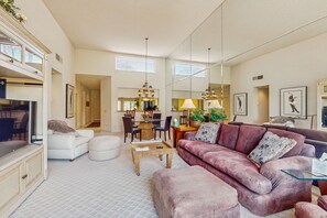 A spacious living room with a large sofa, ottoman, and a coffee table. There is a dining area with chairs and a table in the background. - Inviting PGA West Condo w/3 Golf Courses + Sparkling Pool & Hot Tub (La Quinta)