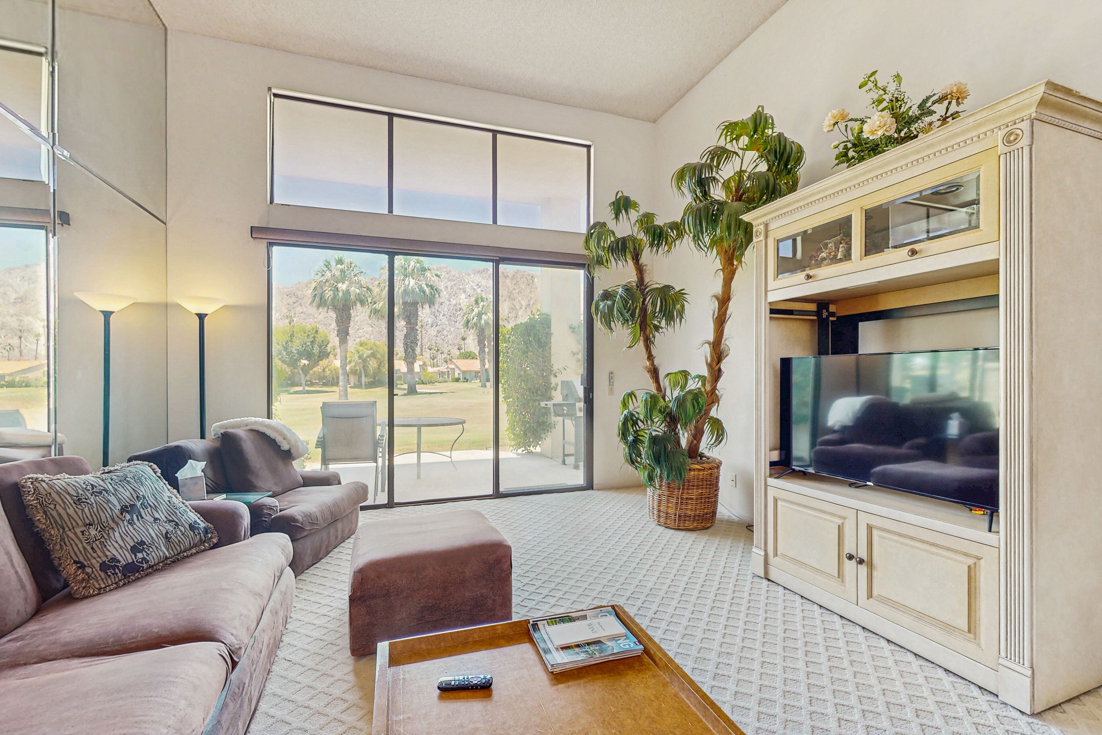 A spacious living room with a large TV, comfortable seating, a coffee table, and a large window offering a view of the outdoors.