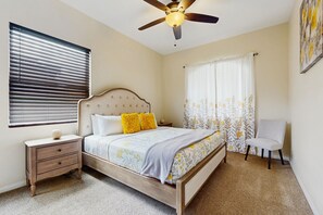 A bedroom with a wooden bed, a nightstand, a chair, a ceiling fan, and a window with blinds. - Desert Bliss: Your Poolside Paradise with Mountain Views, AC, and Wifi. (Cathedral City)